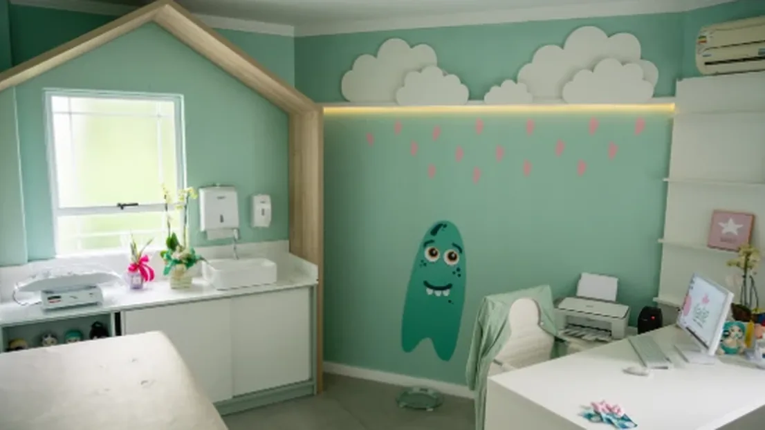 Sala de atendimento da Nanile, com casinha de madeira, nuvens na parede e decoração pensada para crianças